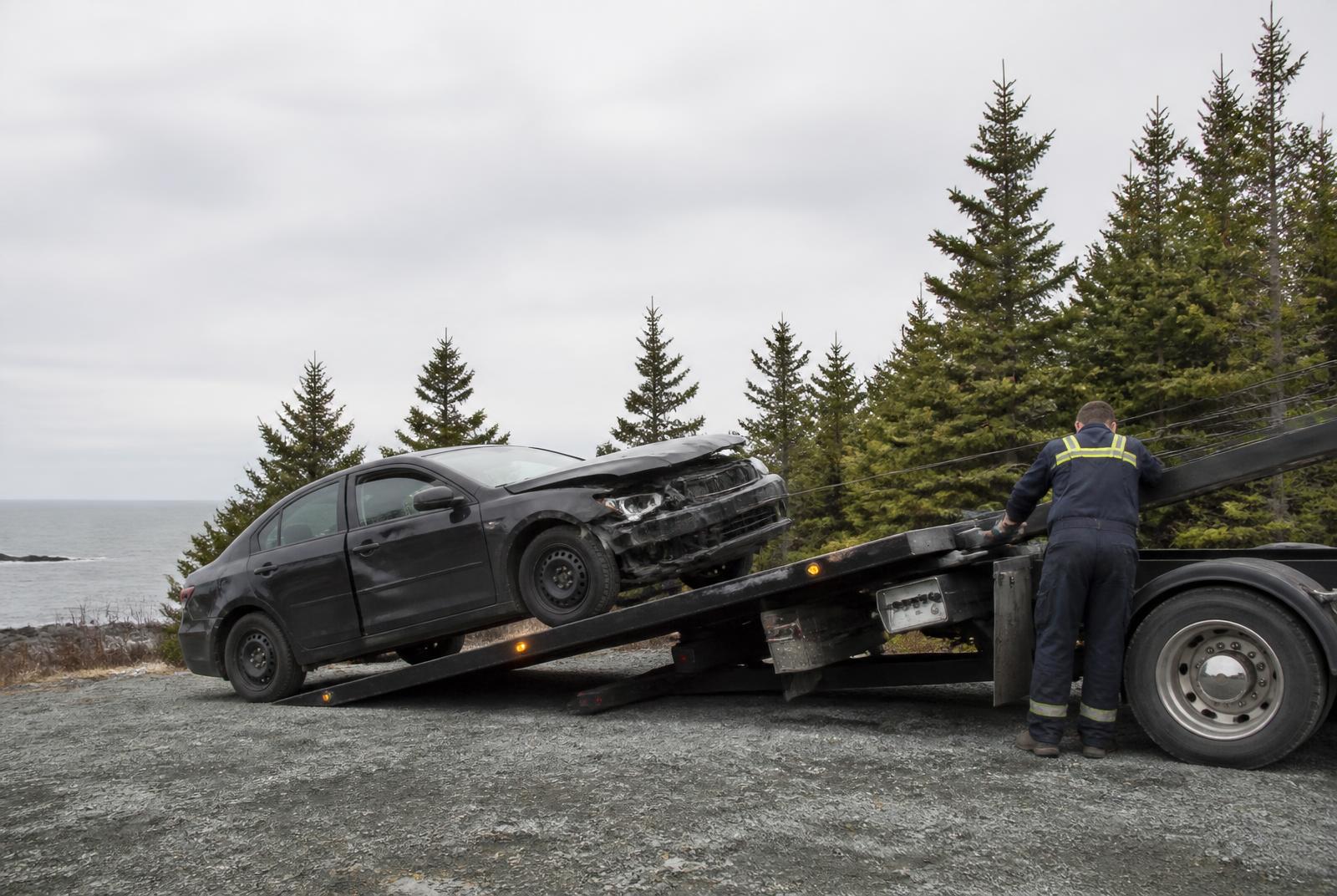 Tow operator loading a damaged car onto a flatbed truck on the Cape Breton coast